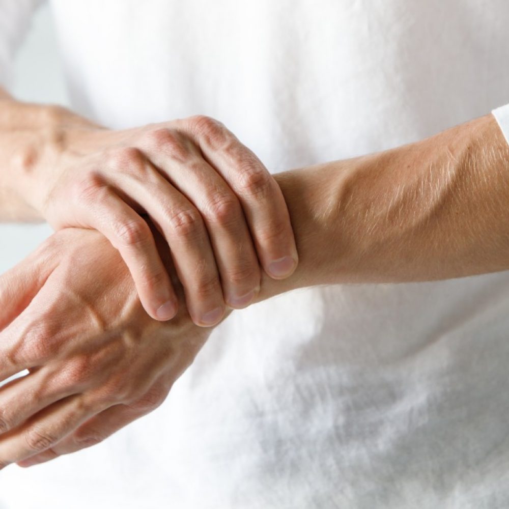 Closeup of male arms holding his painful wrist caused by prolonged work on the computer, laptop. Carpal tunnel syndrome, arthritis, neurological disease concept. Numbness of the hand