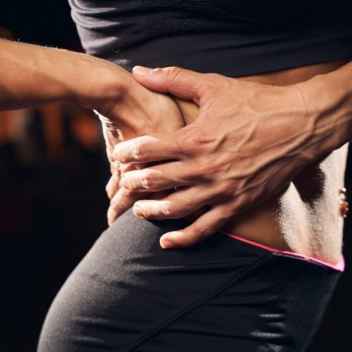Cropped photo of a muscular woman wearing sport clothes holding on to her back at the gym