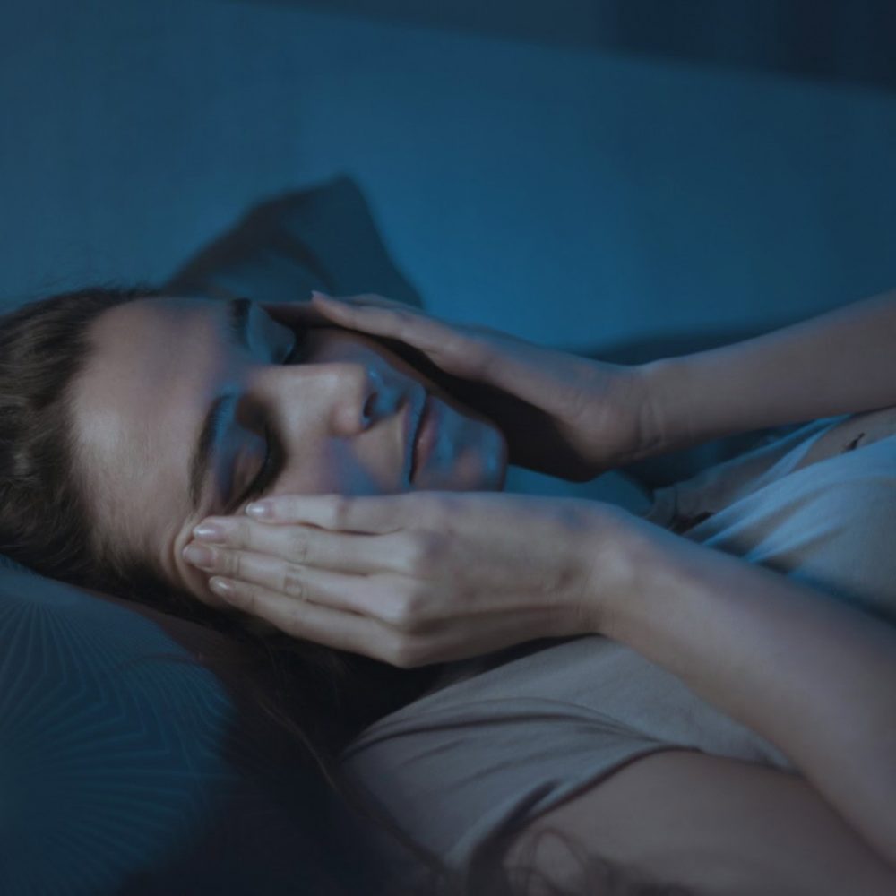Stressed young woman suffering from insomnia, she is lying in bed and touching her face